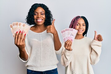 Poster - Beautiful african american mother and daughter holding turkish lira banknotes smiling happy and positive, thumb up doing excellent and approval sign