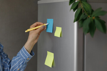 a person makes notes on a sticker on a refrigerator, a reminder from a phone, write by hand, a note on stickers, a note on a sticker, write a reminder, phone in hand, phone reminders, home office