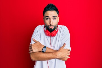 Wall Mural - Young man with beard listening to music using headphones shaking and freezing for winter cold with sad and shock expression on face