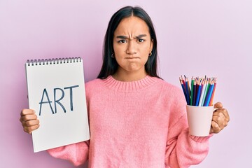 Poster - Young asian woman holding art notebook and colored pencils skeptic and nervous, frowning upset because of problem. negative person.