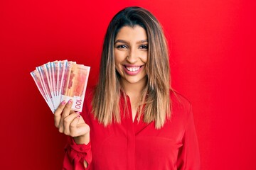 Sticker - Beautiful brunette woman holding 100 norwegian krone banknotes looking positive and happy standing and smiling with a confident smile showing teeth