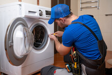 Working Man Plumber Repairs A Washing Machine In Home. Washing Machine Installation Or Repair. Plumber Connecting Appliance