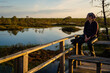 © Volha - A woman admires the landscape of a forest lake among the raised bogs at sunset. A special observation platform for visitors to the reserve.