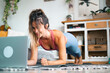 © simona - Young woman exercising at home doing push ups and looking at her personal laptop computer to learn or teach workout - content creator business free healthy lifestyle people concept