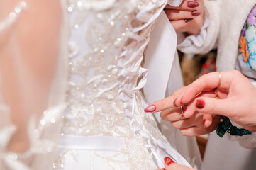 Wall Mural - Bridesmaids tie a bow on the wedding dress. Preparing the bride. Morning of the bride