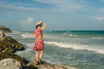 Wall Mural - beautiful girl in a hat and a black dress looks at the ocean. TULUM, Mexico