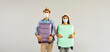 © Studio Romantic - Couple going on a holiday trip. Man and woman in face masks holding suitcases standing isolated on light gray copy space banner background. Concept of people ready for summer vacation and safe travel