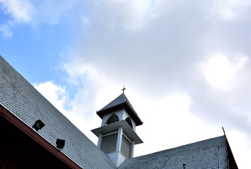 Church Roof with a cross. Church building roof with holy cross. Cloudy moody blue sky background. Minimal architecture design and detail. Exterior design and detail. Abstract architecture.