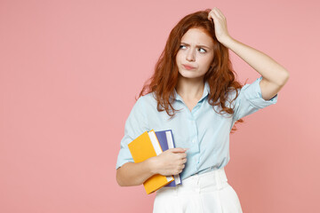 Young pensive puzzled redhead student woman wear blue shirt hold book looking aside sctratch head isolated on pastel pink background studio portrait Education high school university college concept.
