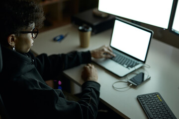 Wall Mural - Young guy wearing glasses sitting at the table in front of many computer monitors and using laptop while working late at night