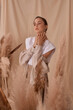 © Dmitry Tsvetkov - Tender soft studio portrait of elegant female model posing between ears of rye at textile background. Girl in brown skirt and beige jacket. Young woman with brunnette hair in pony tail