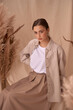 © Dmitry Tsvetkov - Young elegant female model sitting at beige textile background and posing between ears of rye. Brunette girl with makeup and pony tail hair in white shirt and beige skirt and jacket