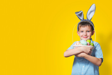 Wall Mural - Cute little child is wearing bunny ears on Easter day and holding basket with painted eggs. Happy kid is holding Easter basket