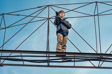 Wall Mural - Fashionable boy ruffer climbs metal structures at heights in an abandoned factory. Dangerous entertainment for children. Parkour. Extreme sports. Danger of walking. Suicide. Troubled teenager. Tomboy