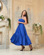 © Dmitry Tsvetkov - Attractive cheerful female model in blue elegant dress standing in bright interior