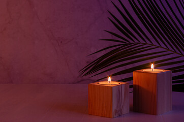 Romantic home decor in tropical style with burning candles and palm leaf in evening purple and orange light, copy space.