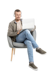 Canvas Print - Young man with laptop listening to music while sitting in armchair on white background