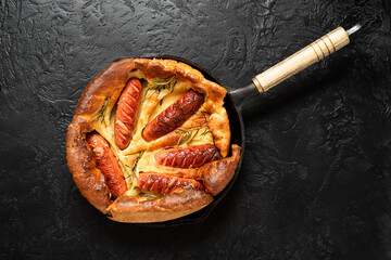 Wall Mural - Toad in the hole, Sausage Toad, traditional English dish of sausages in Yorkshire pudding batter. Black background, top view