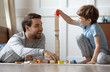 © fizkes - Playful young Caucasian father and little 8s boy child sit on floor at home have fun build construct with wooden blocks bricks. Happy caring dad and small son play together on family weekend.