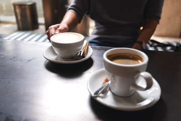 Closeup image of a woman holding a white cup of coffee on the table to drink in cafe