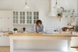© fizkes - Focused young Caucasian woman in headphones busy study online on computer in kitchen at home. Concentrated millennial female in earphones take distant course on laptop write make notes.