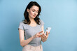 © speed300 - Pretty, young woman enjoys cellphone isolated on blue background. Beautiful girl on a background of blank wall, copy space.