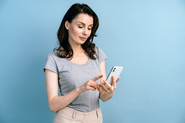 Pretty, young woman enjoys cellphone isolated on blue background. Beautiful girl on a background of blank wall, copy space.