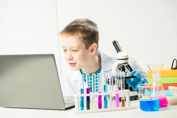 Wall Mural - schoolboy with a laptop in the laboratory conducts chemical experiments with substances in test tube