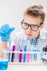 Wall Mural - a schoolboy studies multi-colored substances in test tubes, conducts experiments - a portrait on a w