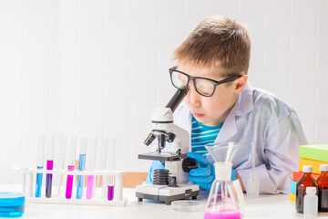Wall Mural - a schoolboy with a microscope examines chemicals in test tubes, conducts experiments - a portrait on