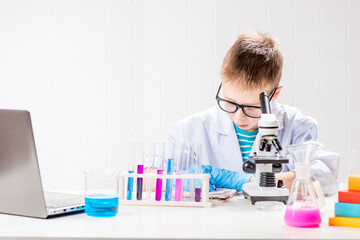 Wall Mural - a schoolboy with a microscope examines chemicals in test tubes, conducts experiments - a portrait on
