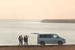 The four friends standing near the minivan against the sunset sky