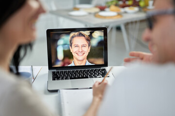 Cheerful marriage counselor smiling to his clients, using video chat app, giving online help during lockdown. Focus on laptop screen