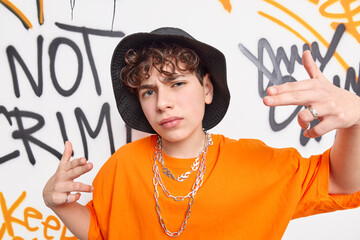 Sticker - Yo yo look at me. Cool boy teenager with curly hair dressed in stylish clothes being street artist or rapper wears hat t shirt chains on neck poses against graffiti wall in urban area. Swag.