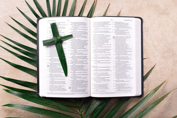 Palm Sunday concept. Palm cross on open Holy Bible and palm leaves. Reminder of Jesus sacrifice and Christ resurrection. Easter passover. Eucharist concept. Christianity symbol and faith