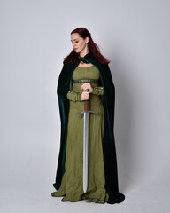 Poster - full length portrait of red haired girl wearing celtic, green medieval gown with fantasy velvet cloak. Standing pose isolated against a studio background.