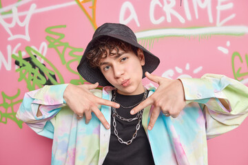 Sticker - Yo look at me. Self satisfied cool fourteen years old guy males rap gesture wears fashionable clothes poses at street against creative colorful graffiti wall. Youth and urban lifestyle concept