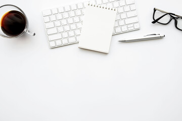 small blank notebook is in top of computer keyboard over with office desk table with pen and cup of 