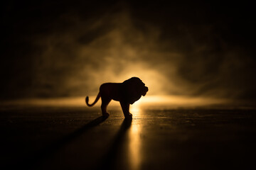 Wall Mural - A silhouette of lion miniature standing on wooden table. Creative decoration with colorful backlight with fog. Selective focus