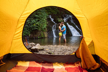 Poster - couple standing in the lake waterfall on background view from yellow camping tent