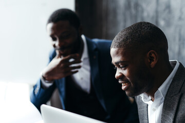 Wall Mural - Serious african american men at conference talking to each other while sitting at the table and working at the laptop