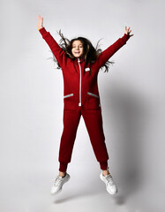 Happy smiling joyful caucasian preteen girl model in comfortable tracksuit jumping with raised arms looking at camera isolated on copy space. Portrait on studio background. Advertisement concept