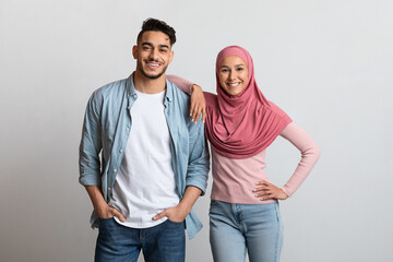 Happy arab man and young woman in hijab posing over gray background