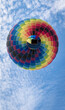 Ein Heißluftballon fliegt als bunter Punkt genau von unten gegen den blauen Himmel mit weißen Wölkchen gesehen