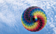 Ein Heißluftballon als bunter Punkt genau von unten gegen den blauen Himmel mit weißen Wölkchen gesehen