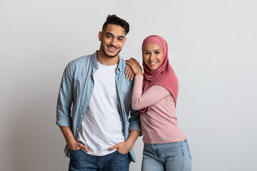 Wall Mural - Modern muslim couple man and woman in hijab posing on gray background