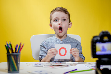 Beautiful little blogger bloging about learning the alphabet on yellow background. Back to school. Distance learning online education.