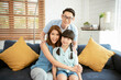 © NaMong Productions - Happy Asian family hugging together on sofa at home living room.