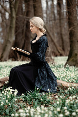 Sticker - girl in vintage dress with book is sitting on meadow with snowdrops in the forest