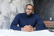 © Vadim Pastuh - Head shot portrait of confident African American businessman wearing glasses sitting at work desk with laptop, excited freelancer looking at camera, adult student working on online research project